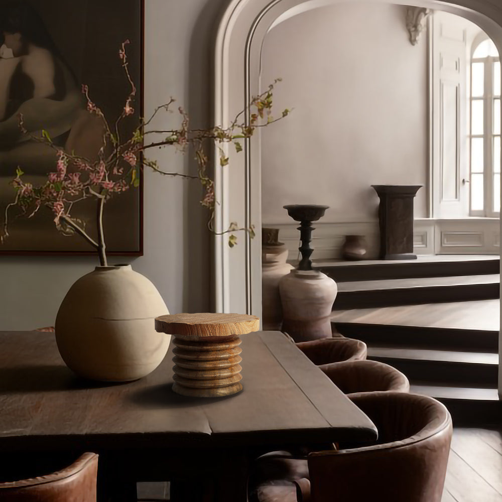 Lemieux et Cie Seraphin Pedestal with stacked tripod form, displayed on table beside spherical vase in a light-filled dining room with arched mirror and neutral walls.