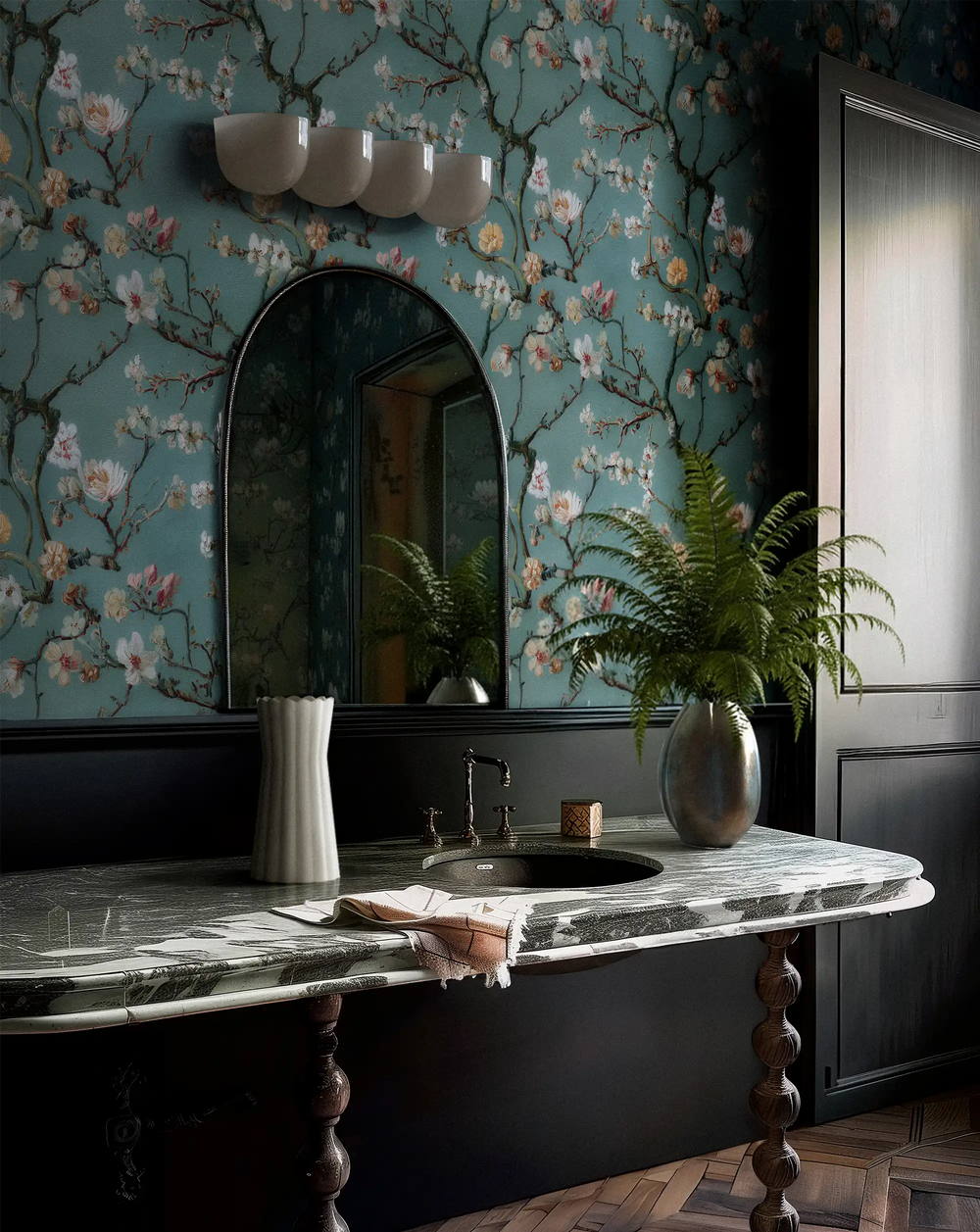 Lemieux et Cie Sky Blooms Wallpaper in aqua with blossoms and branches, bathroom with marble-topped vanity, arched mirror, and dark wainscoting.