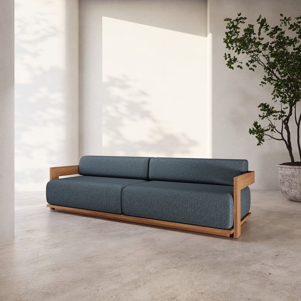 Lemieux et Cie S2 Teak 95" Sofa in charcoal upholstery with angular wood frame, shown in sunlit room with neutral plaster walls and stone flooring.