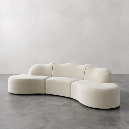 Lemieux et Cie Serpentine Sectional Sofa in ivory upholstery, modular curved three-piece sofa on polished concrete floor against textured plaster walls.