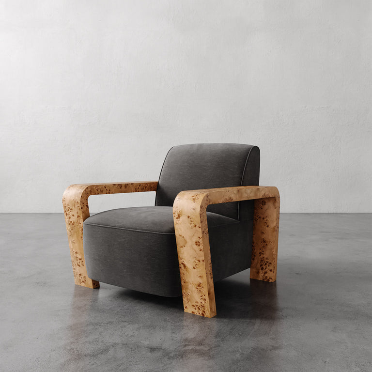 Lemieux et Cie Dumas Chair with sculptural blonde burl arms and charcoal upholstered seat, lounge chair on concrete floor against neutral plaster walls.
