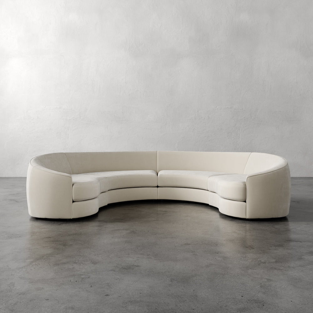 Lemieux et Cie Rulmann 4-Piece Sectional in ivory, curved modular sofa with rounded arms, shown on polished concrete floor against textured plaster walls.
