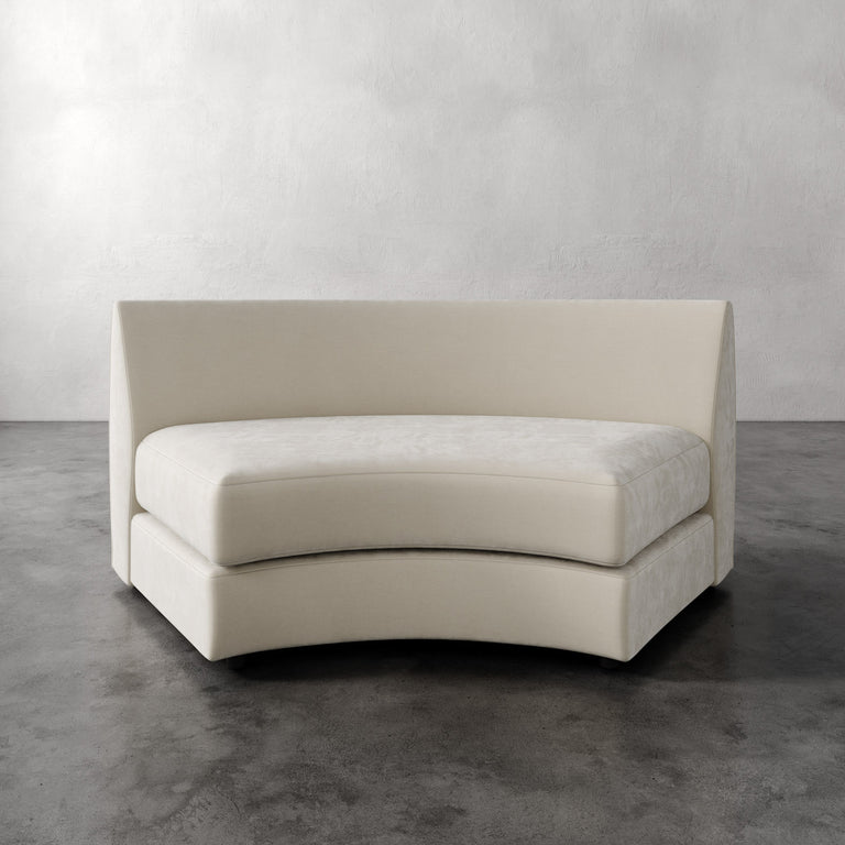 Lemieux Et Cie Rulmann Wedge Beige curved sofa on a gray floor with a white wall background