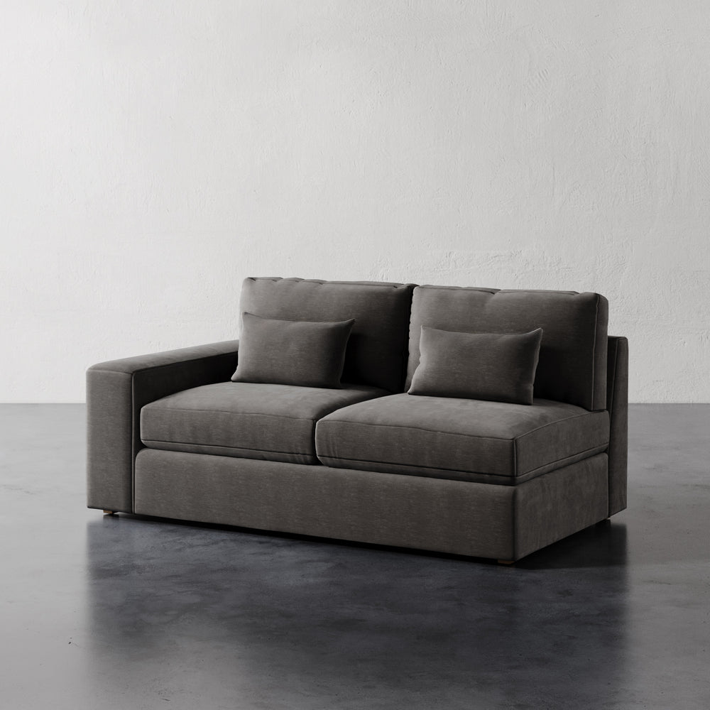 Lemieux et Cie Lacroix Left or Right Arm Loveseat, modular sofa with clean rectilinear form, shown on dark stone floor against white plaster walls.