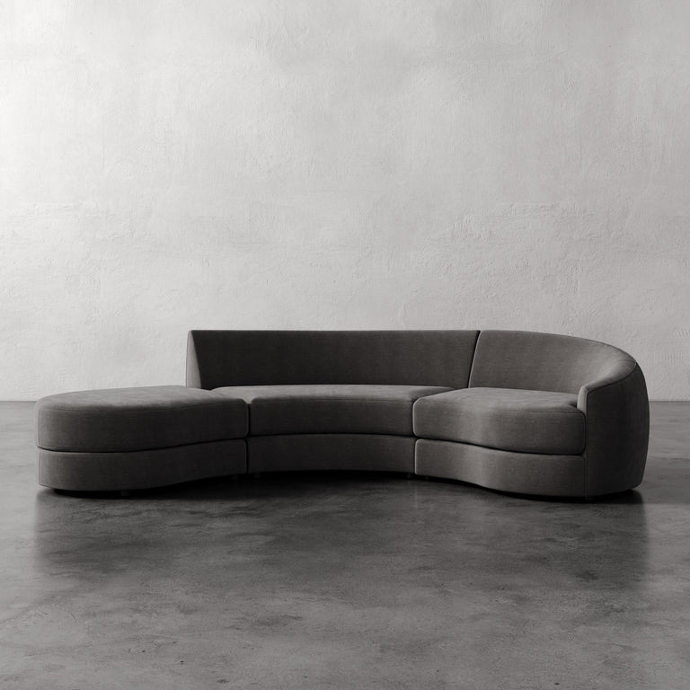 Lemieux Et Cie Rulmann 3-Piece Right Sectional Gray curved sofa on a concrete floor with a plain white wall background