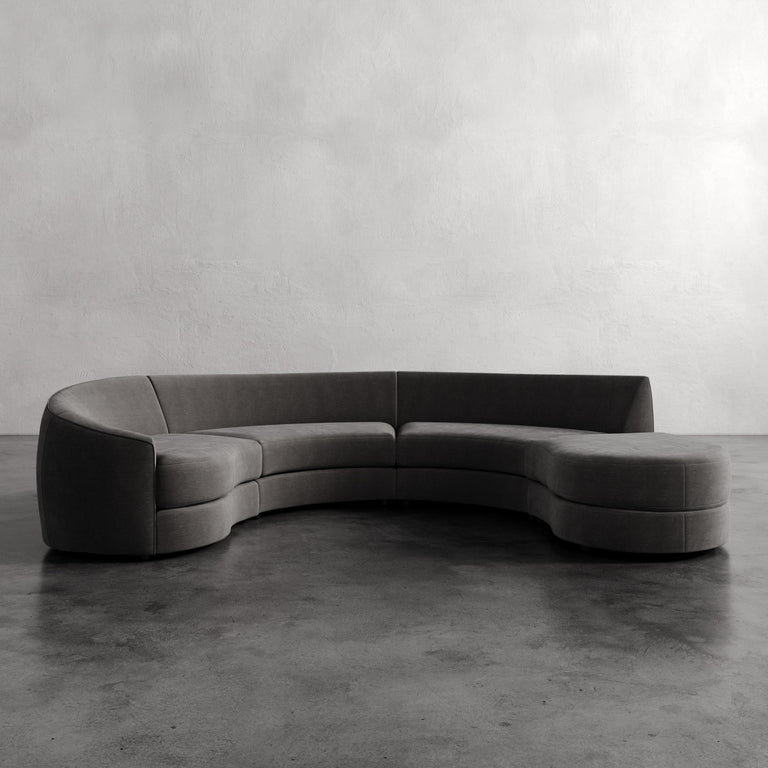 Lemieux Et Cie Rulmann 4-Piece Left Sectional Gray curved sofa in a minimalistic room with a plain wall and concrete floor.