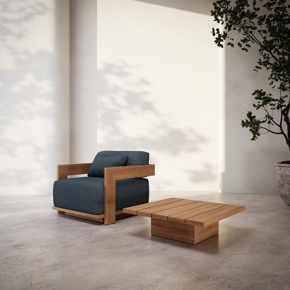 Lemieux et Cie S2 Teak square side table in solid teak wood, paired with lounge chair on concrete floor against white walls in soft daylight.