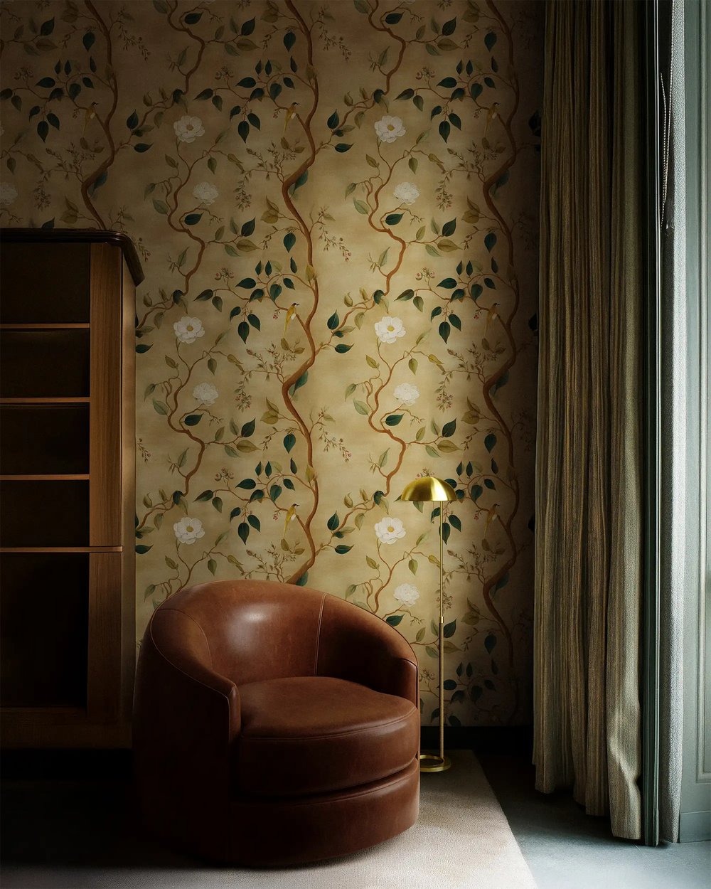 Lemieux et Cie Treillage Gold Wallpaper in warm gilded surface with branches and blossoms, shown in sitting room with leather chair, wood shelving and draped curtains.