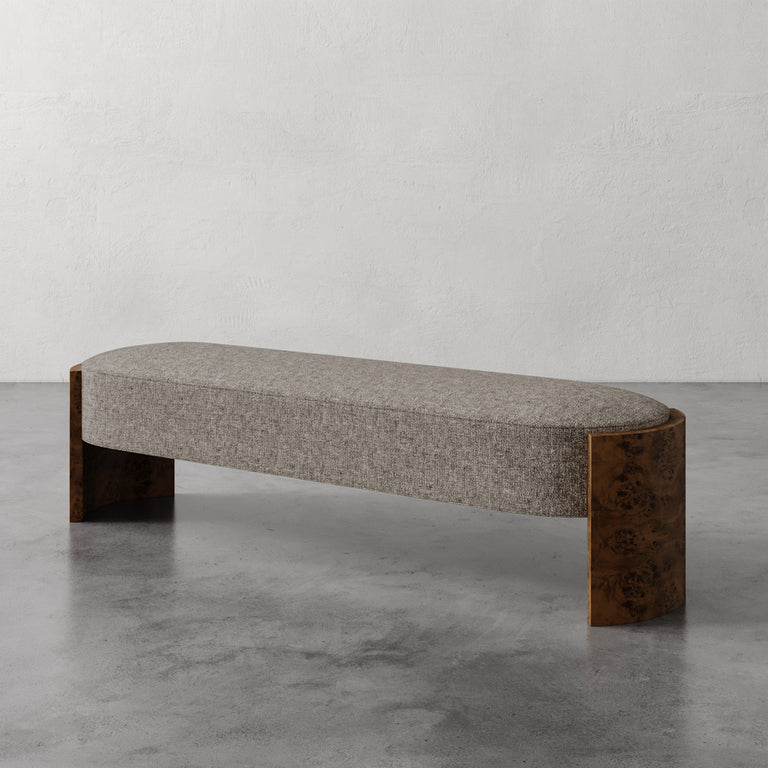 Lemieux et Cie Benoit Custom Upholstered Bench with textured taupe upholstery and curved Maple burl legs, shown on concrete floor against neutral plaster wall.