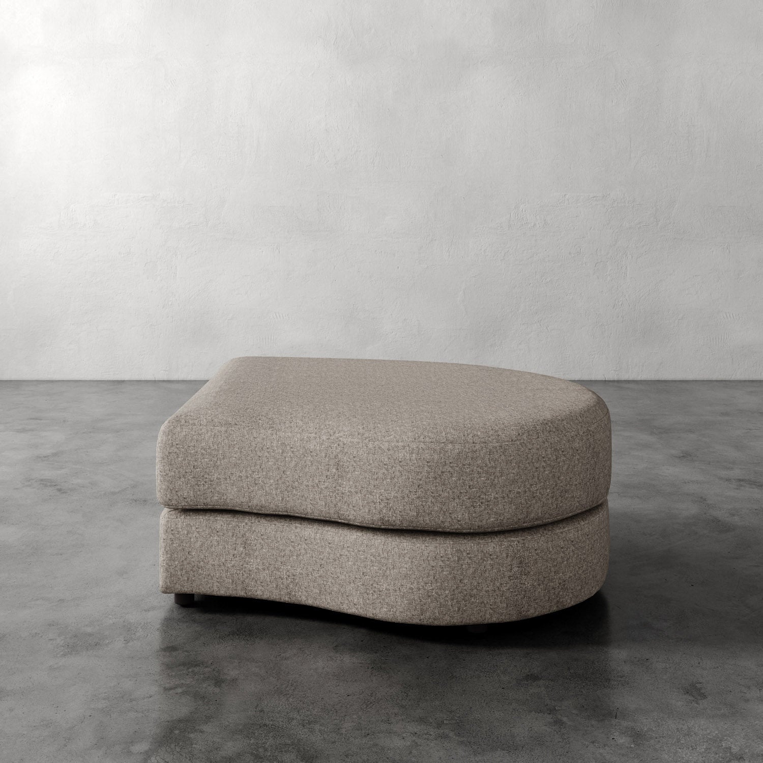 Lemieux Et Cie Rulmann Right Ottoman Beige ottoman on a gray concrete floor with a white wall background