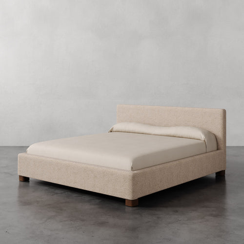 Lemieux et Cie Gérard Bed, low-profile platform bed with wrapped headboard and rounded block feet, shown on polished concrete floor against neutral plaster walls.