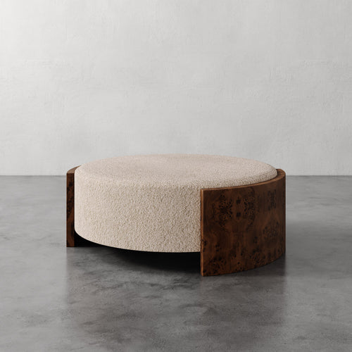Lemieux et Cie Benoit Coffee Table Ottoman in ivory bouclé with wire-brushed oak curved frame, shown on polished concrete floor against neutral plaster wall.