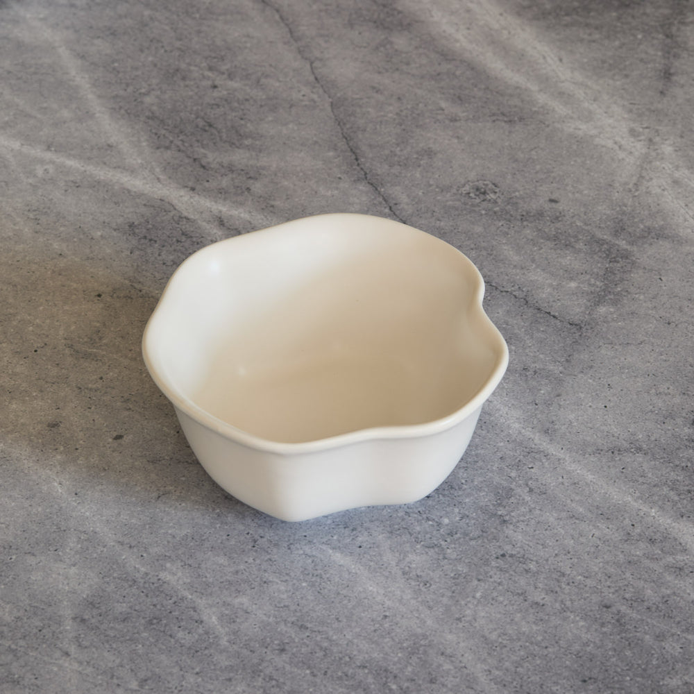 Lemieux et Cie Amorphous Bowl in soft white matte glaze, stoneware bowl with organic asymmetrical curves, shown on textured gray stone surface.