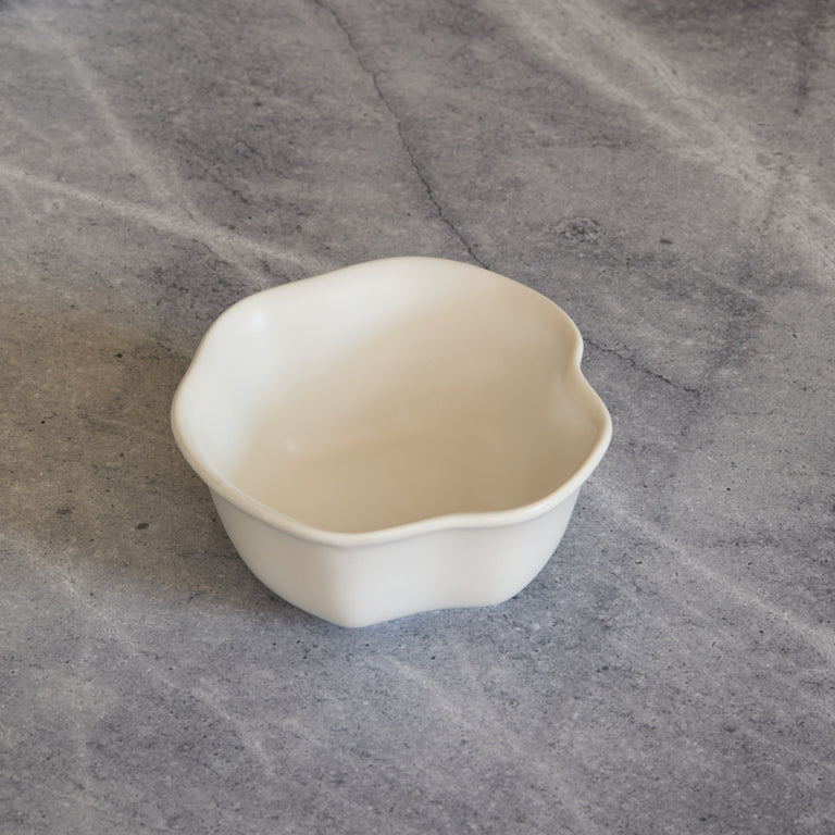 Lemieux et Cie Amorphous Bowl in soft white matte glaze, stoneware bowl with organic asymmetrical curves, shown on textured gray stone surface.