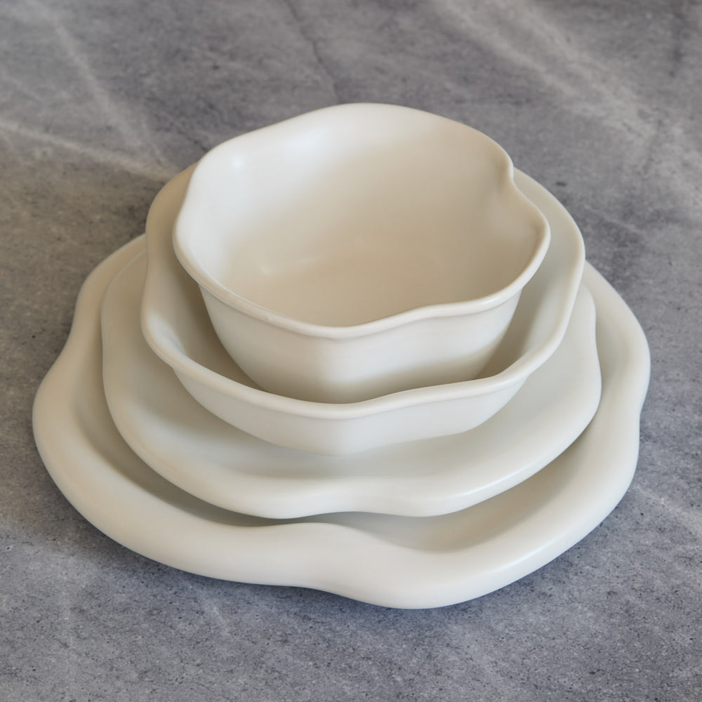 Lemieux et Cie Amorphous Dinnerware Set in soft white matte glaze, stacked stoneware plates with organic curves, shown on grey stone surface.