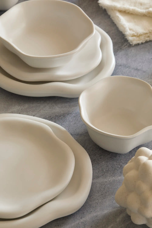 Lemieux et Cie Amorphous Dinnerware Set in soft white matte stoneware, organic curved plates and bowls arranged on gray stone surface with linen.