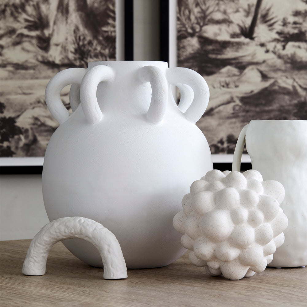 Lemieux et Cie Rhône Vase with oversized circular handles, sculptural ceramic vessel in matte white finish, styled on wood surface with decorative objects and botanical wallcovering.