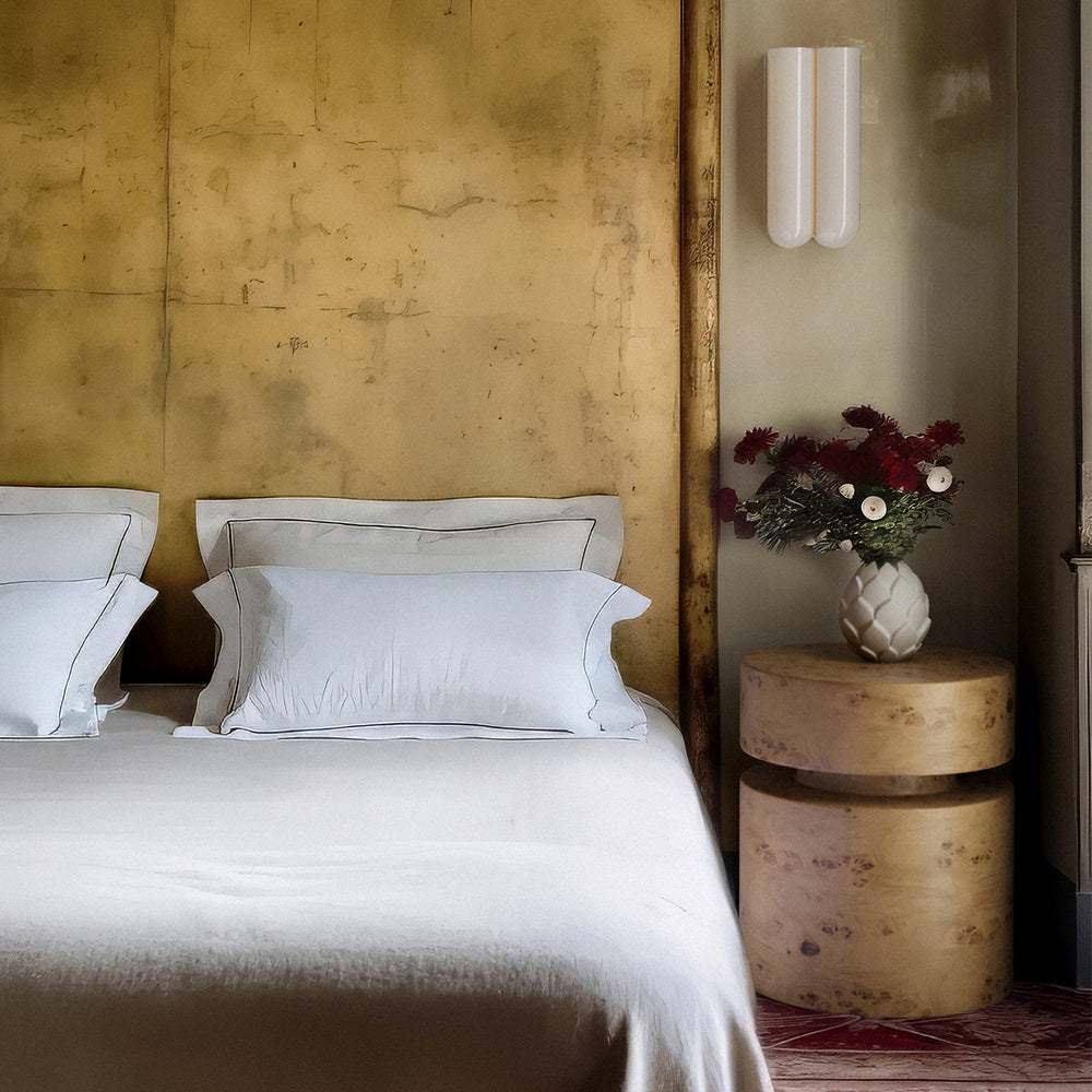 Lemieux et Cie Modernist Ceramic Vase, handmade white ceramic vessel with artichoke-inspired form, styled bedside against aged plaster walls with stacked cylindrical nightstand.