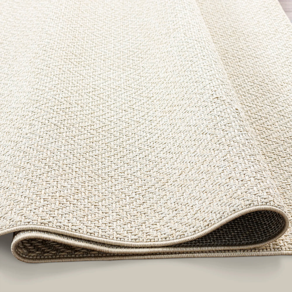 Lemieux et Cie Provence Outdoor Rug in ivory, woven flat-weave rug showing rolled edge detail, on white studio backdrop.