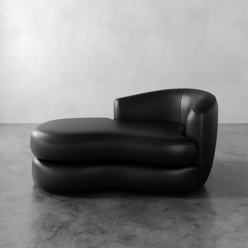 Lemieux et Cie Rulmann Leather Right Arm Chaise in black leather, sculptural low-slung chaise with rounded organic form, on concrete floor against plaster wall.