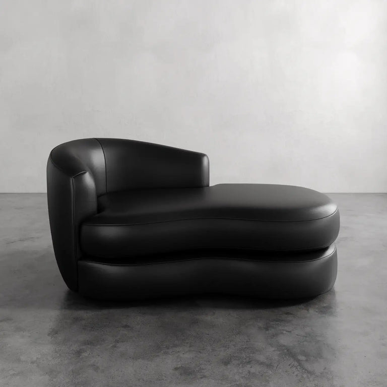 Lemieux et Cie Rulmann Leather Left Arm Chaise in black leather, sculptural low-slung chaise with curved form, shown on polished concrete floor against neutral wall.