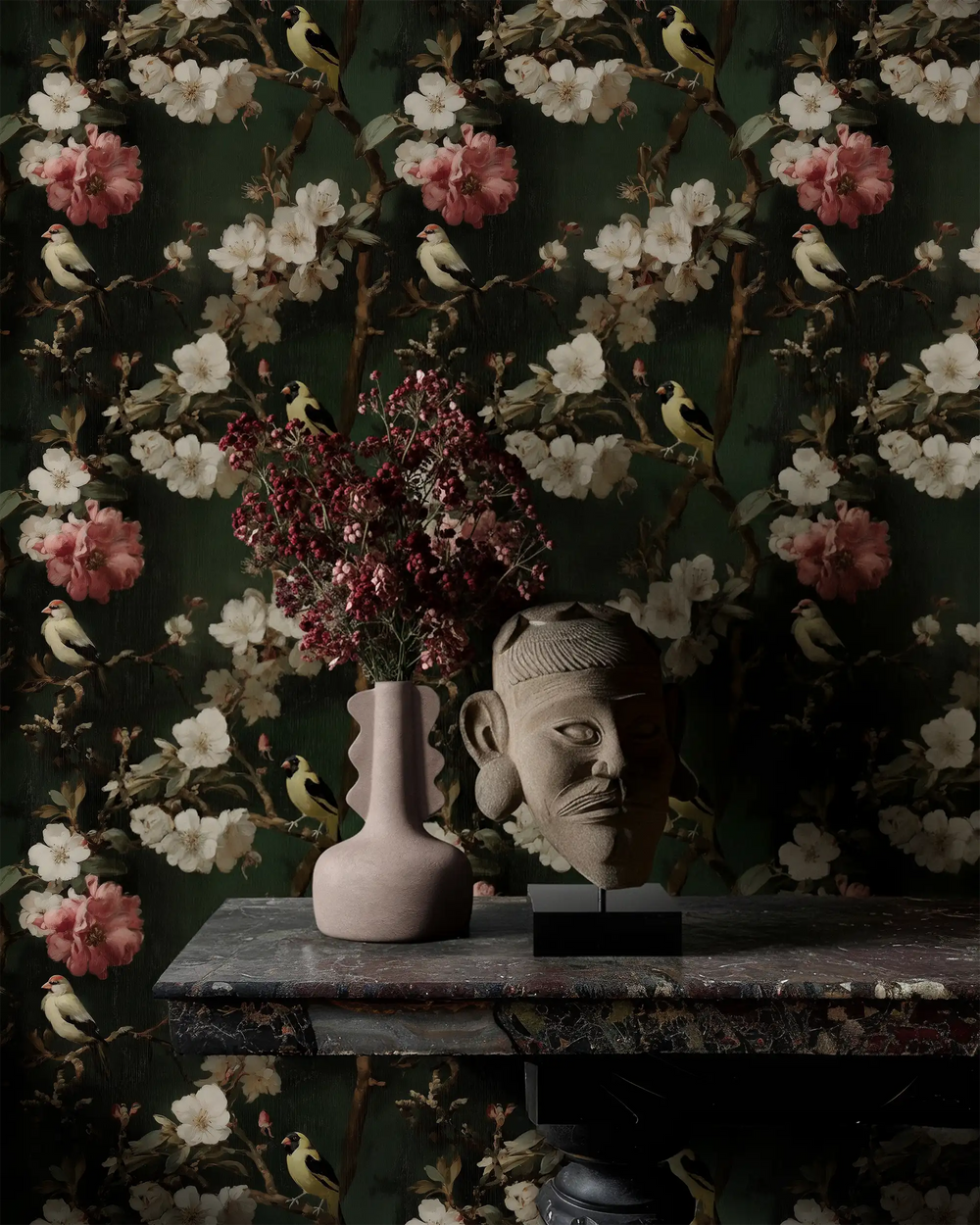 Decorative head sculpture and vase with floral arrangement set against Lemieux et Cie Canary Blossom green chinoiserie wallpaper, featuring dark floral birds inspired by de Gournay style wallpaper.