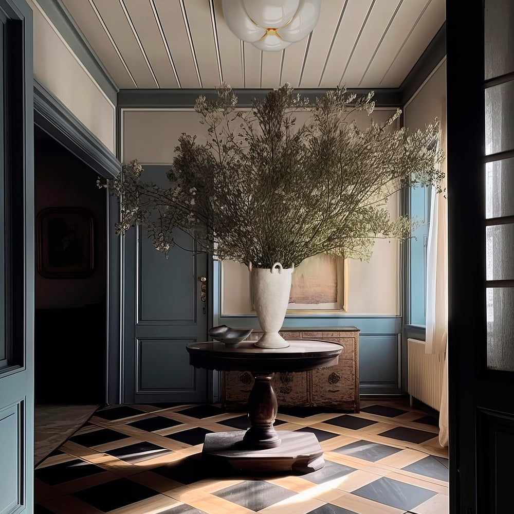 Lemieux et Cie Louis Vase in white ceramic with organic sculptural form, holding dried branches on a round pedestal table in a paneled entryway with geometric inlay floors.