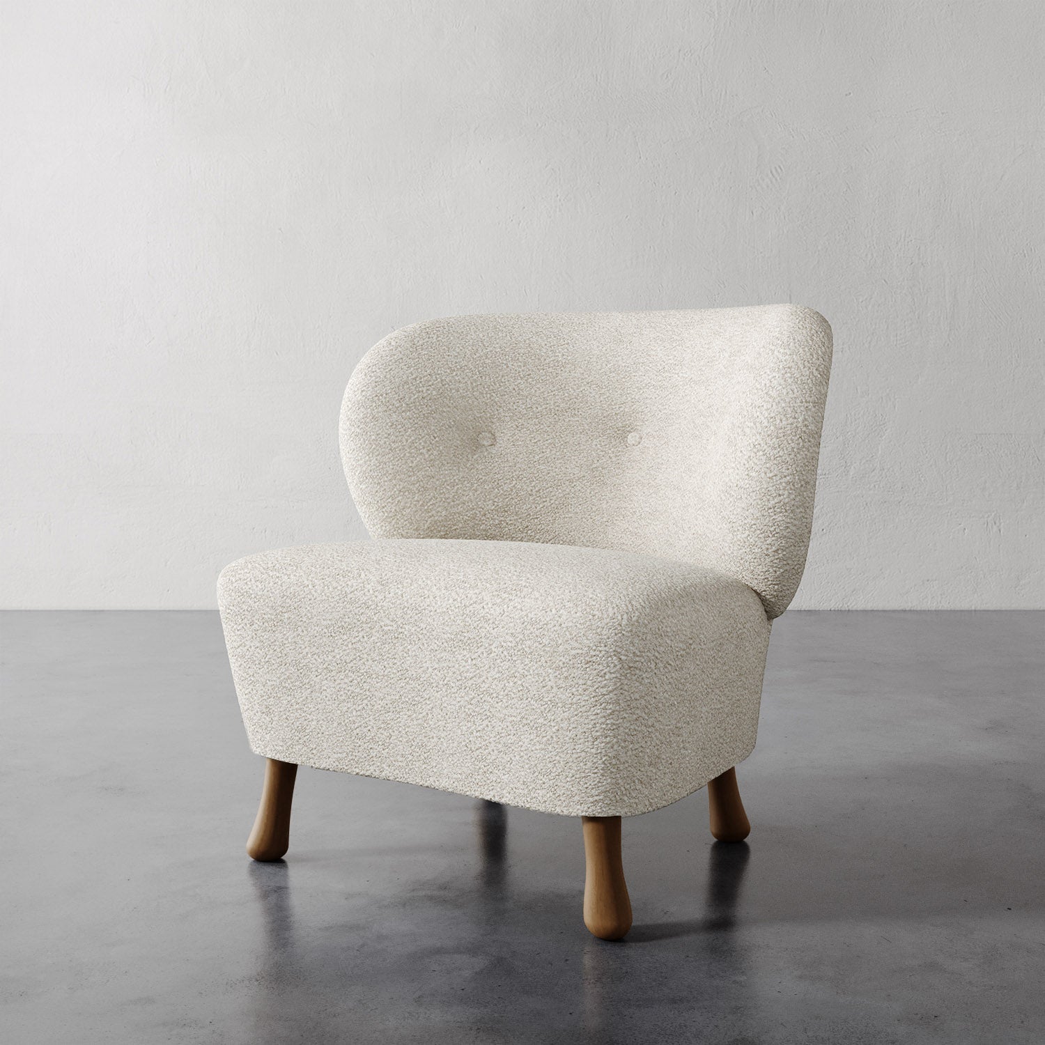 Lemieux et Cie Tourenne Chair in ivory bouclé with tapered wood legs, sculptural lounge chair shown on concrete floor against textured plaster walls.