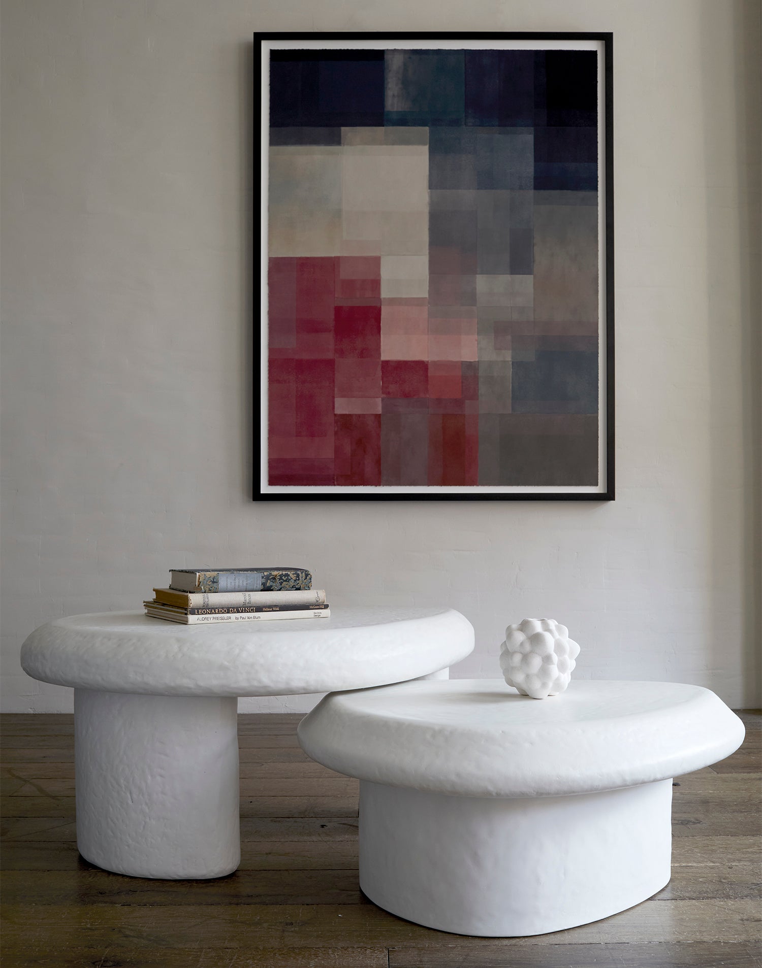 Lemieux et Cie Champ De Couleur 1 fine art print with overlapping geometric blocks in burgundy, navy and neutral tones, framed above sculptural stone tables in a sitting room with neutral walls and wood floors.