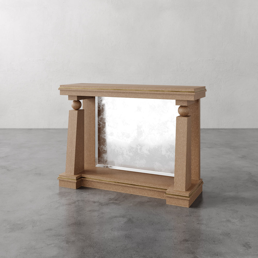 Lemieux et Cie Corvaux Console Table, architectural form with turned sphere details and mirrored panel, shown on polished concrete floor against textured plaster walls.