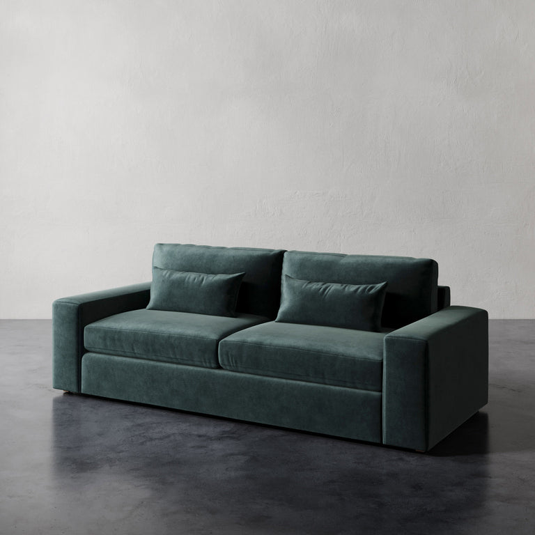 Lemieux et Cie Lacroix Sofa in deep teal upholstery, sofa with bolster pillows on dark concrete floor against textured plaster walls