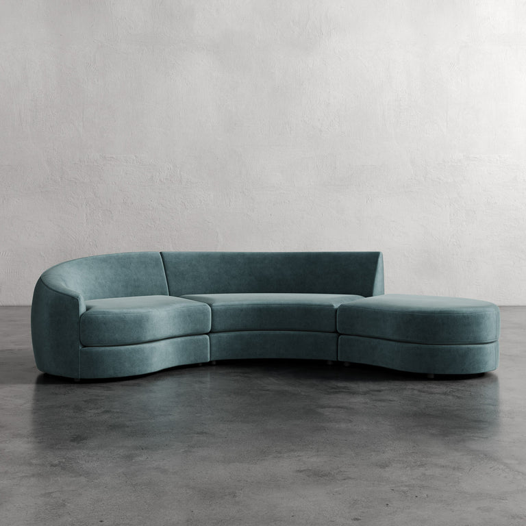 Lemieux et Cie Rulmann 3-Piece Left Sectional in teal upholstery, curved modular sofa with chaise, shown on polished concrete floor against textured plaster walls.