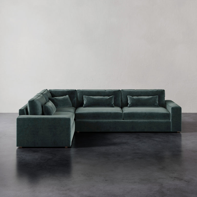 Lemieux et Cie Lacroix Right Arm Sectional in deep green velvet, modular sofa with bolster pillows, on dark concrete floor against neutral walls