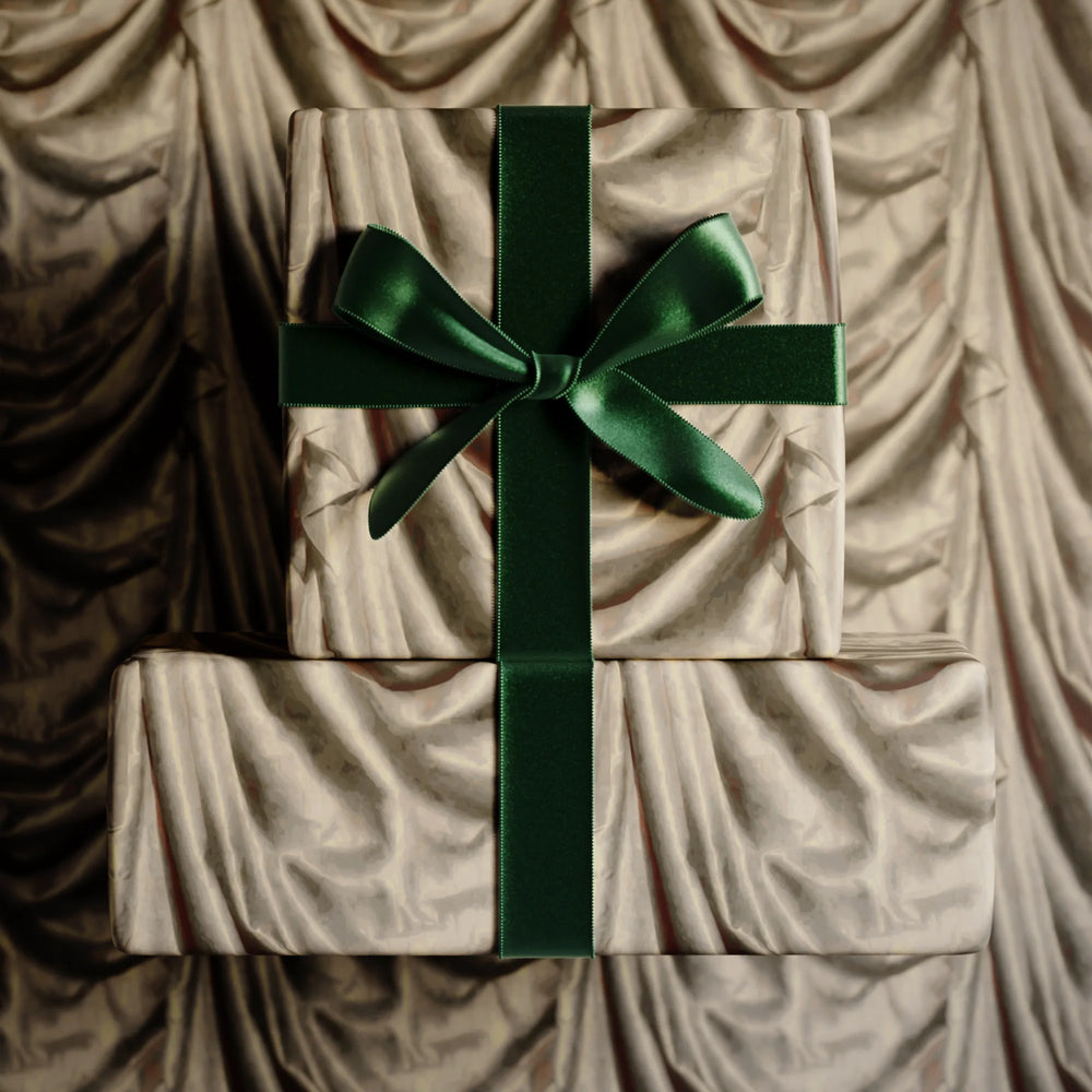 Lemieux et Cie gift wrapping in ivory with emerald green satin ribbon and bow, draped against soft neutral backdrop.