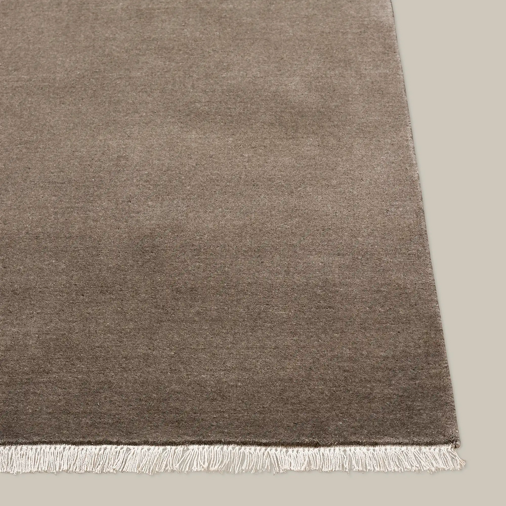 Lemieux et Cie Plume Handmade Wool Rug in taupe, handloomed rug with fringe detail, shown on neutral studio floor.