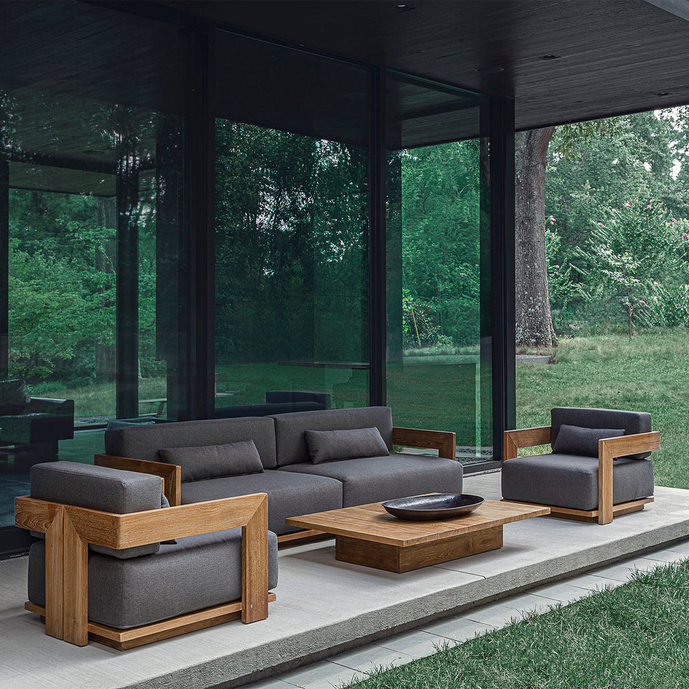 Lemieux et Cie S2 Teak Rectangular Coffee Table in solid teak with dark cushioned seating, outdoor collection on stone terrace overlooking wooded lawn.
