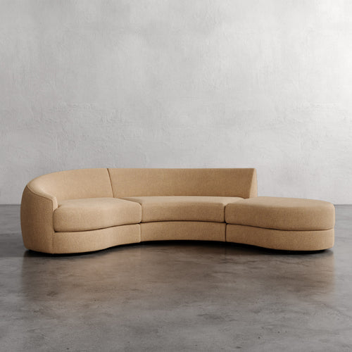 Beige curved sofa on a gray floor with a plain wall background_ Rulmann 3-Piece Left Sectional Golden Rod