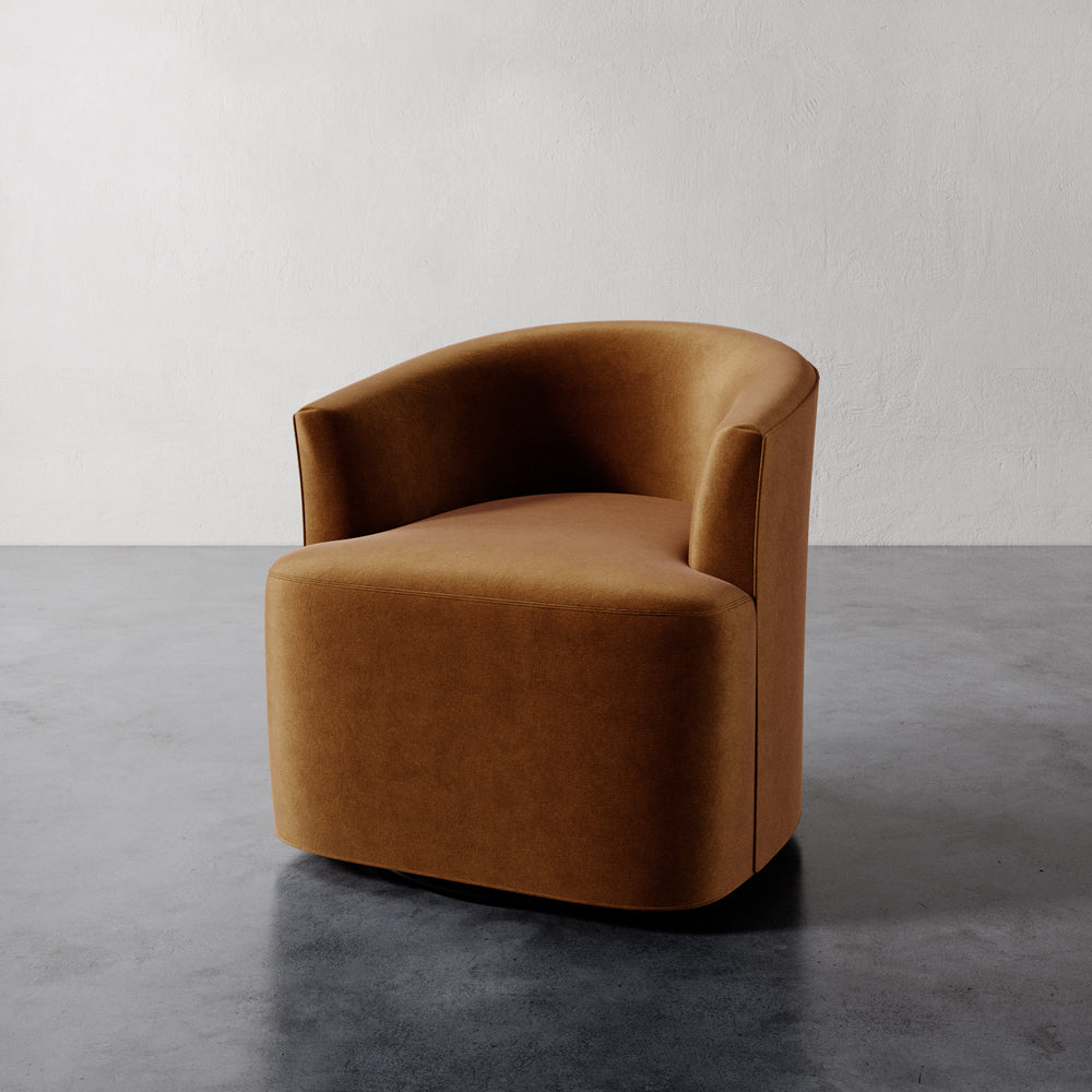 Lemieux et Cie Garnier Swivel Chair in warm camel upholstery, rounded sculptural form on polished concrete floor against textured plaster wall.