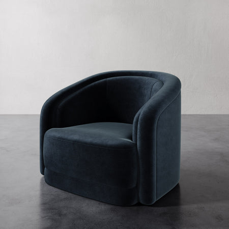 Lemieux et Cie Valence Swivel Chair in deep blue, barrel-back lounge chair with rounded sculptural form, on dark concrete floor against neutral walls.