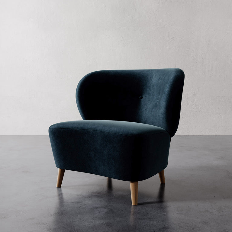 Lemieux et Cie Tourenne Chair in deep teal velvet upholstery with tapered legs, organic rounded silhouette on concrete floor against textured plaster wall.