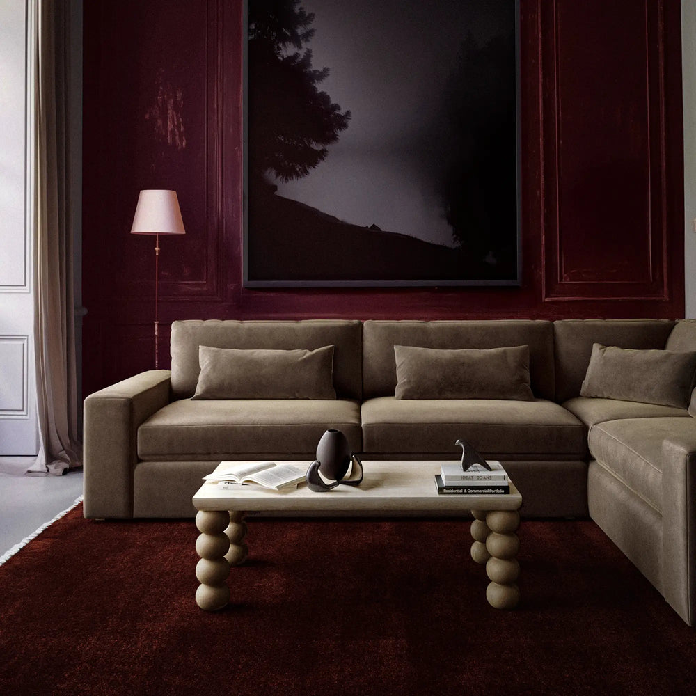 Lemieux et Cie Lacroix Left Arm Sectional, modular sofa in taupe with bolster pillows, styled in sitting room with burgundy paneled walls and deep burgundy rug.