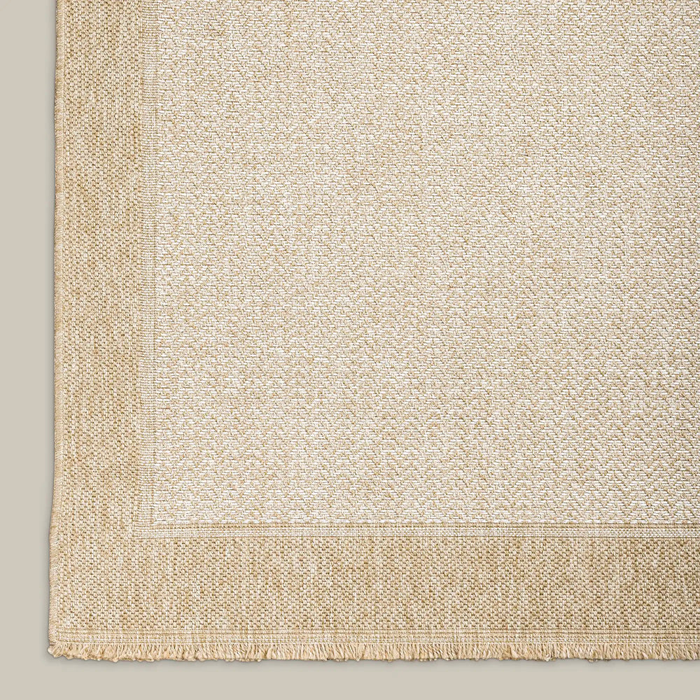 Lemieux et Cie Malika Outdoor Rug in natural tones with textured weave and border detail, shown on neutral studio backdrop.