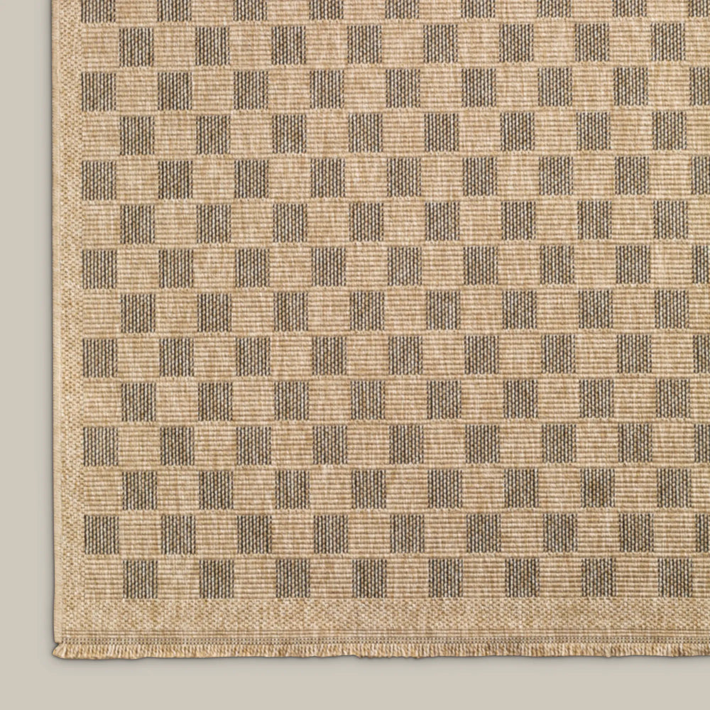 Lemieux et Cie Carreaux Outdoor Rug in natural and black, woven checkerboard pattern, shown on neutral backdrop with corner detail visible.