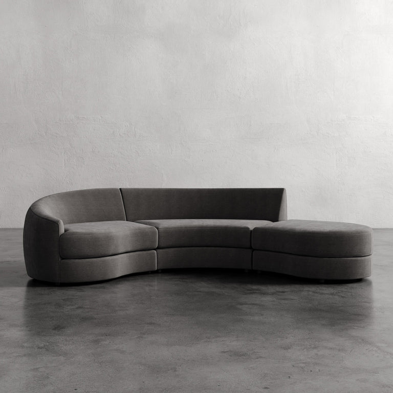 Curved gray sofa against a plain wall. Rulmann 3-Piece Left Sectional Mink Strie