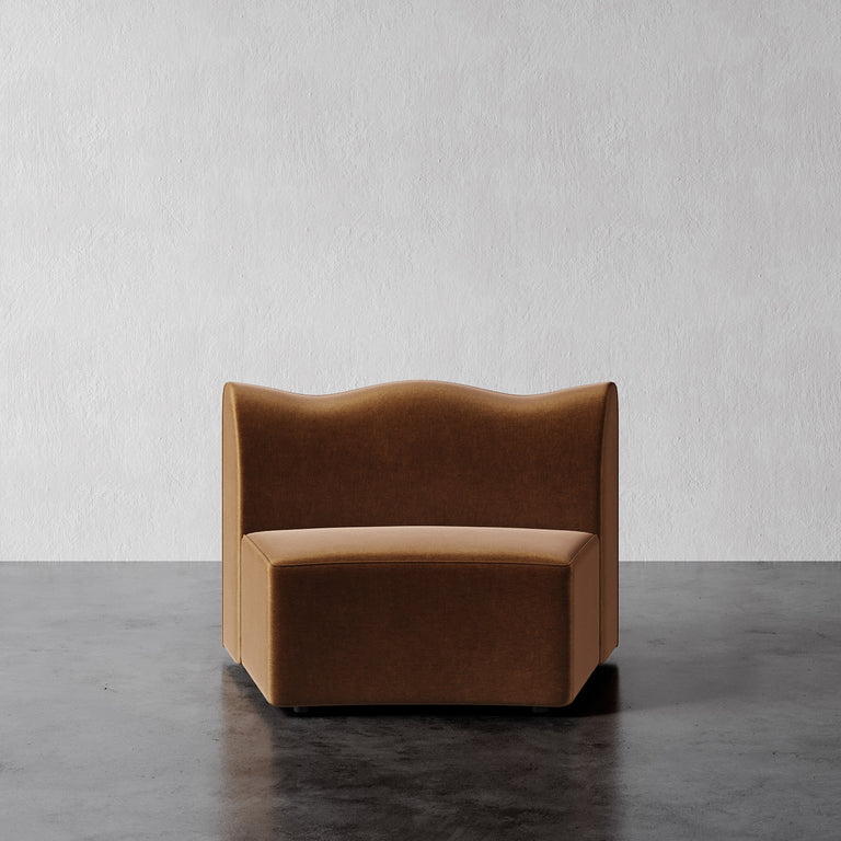 Lemieux Et Cie Serpentine Armless Wedge Brown curved chair on a gray floor with a white wall background.