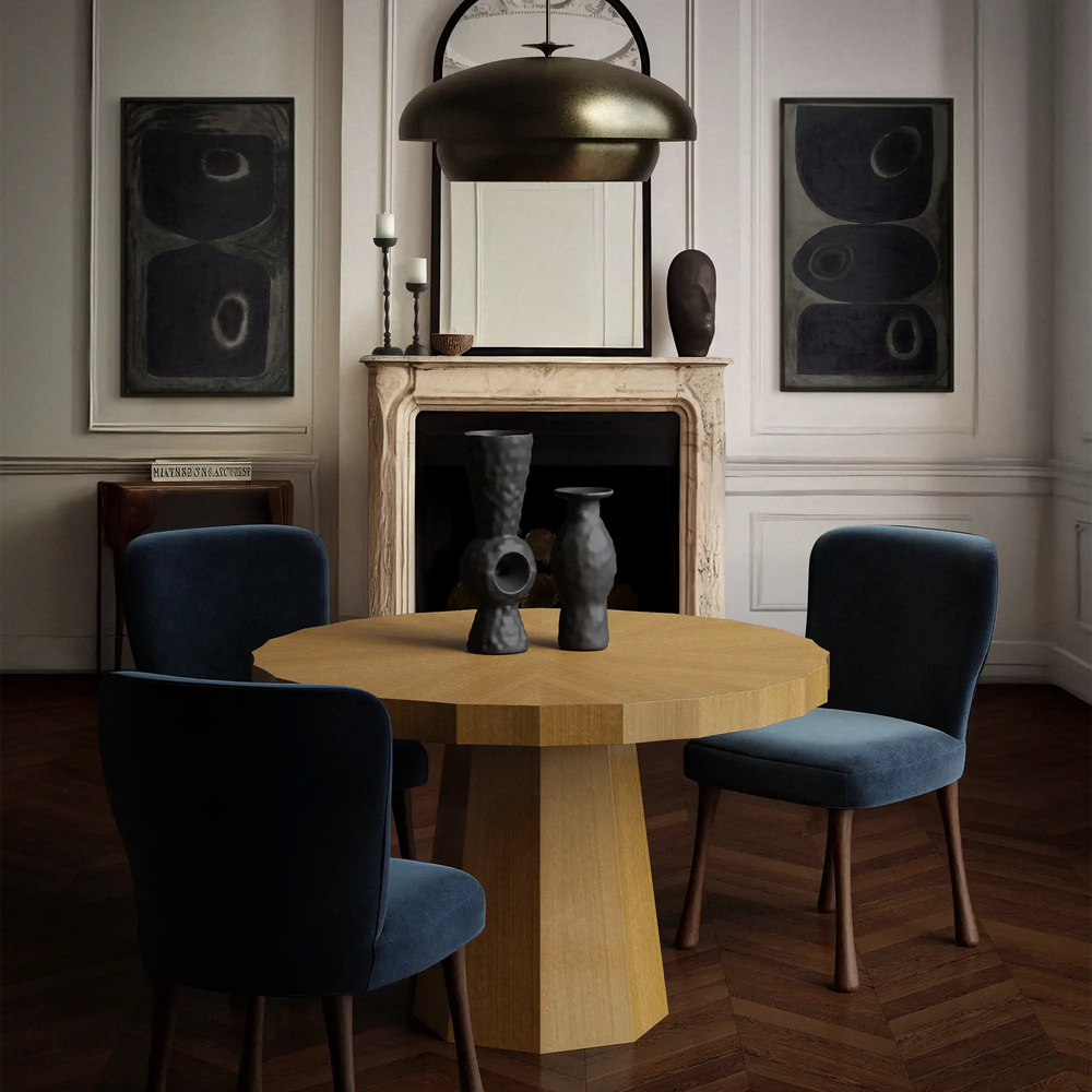 Lemieux et Cie Ondara Fluted Dining Table in champagne eucalyptus with radial marquetry top, round table centered in white-paneled room with stone fireplace mantel and wood floors.