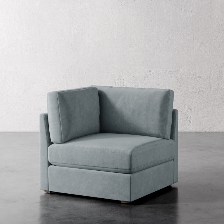 Lemieux Et Cie Chanaux Corner Chair Gray armchair on a gray floor with a white textured wall background