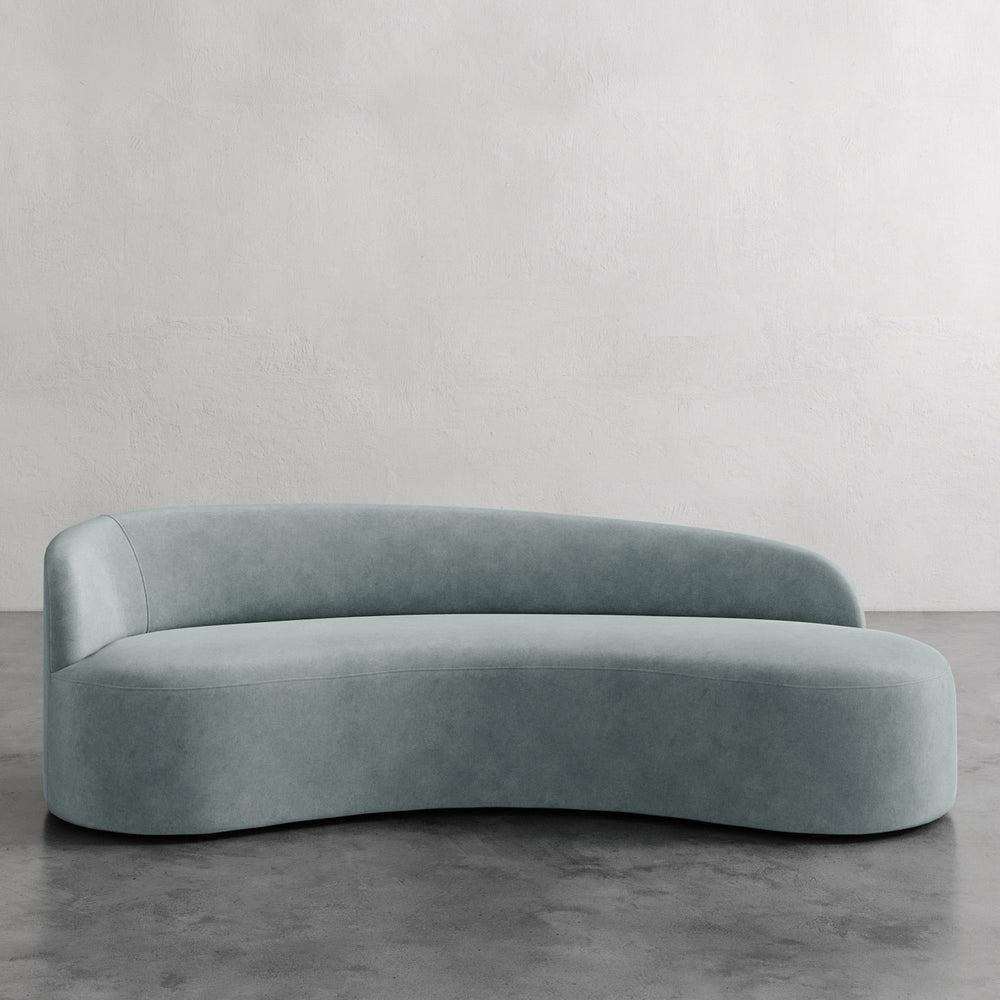 Lemieux et Cie Colette Left Arm Sofa in seafoam green, curved asymmetric sofa with organic silhouette, shown on concrete floor against neutral plaster walls.