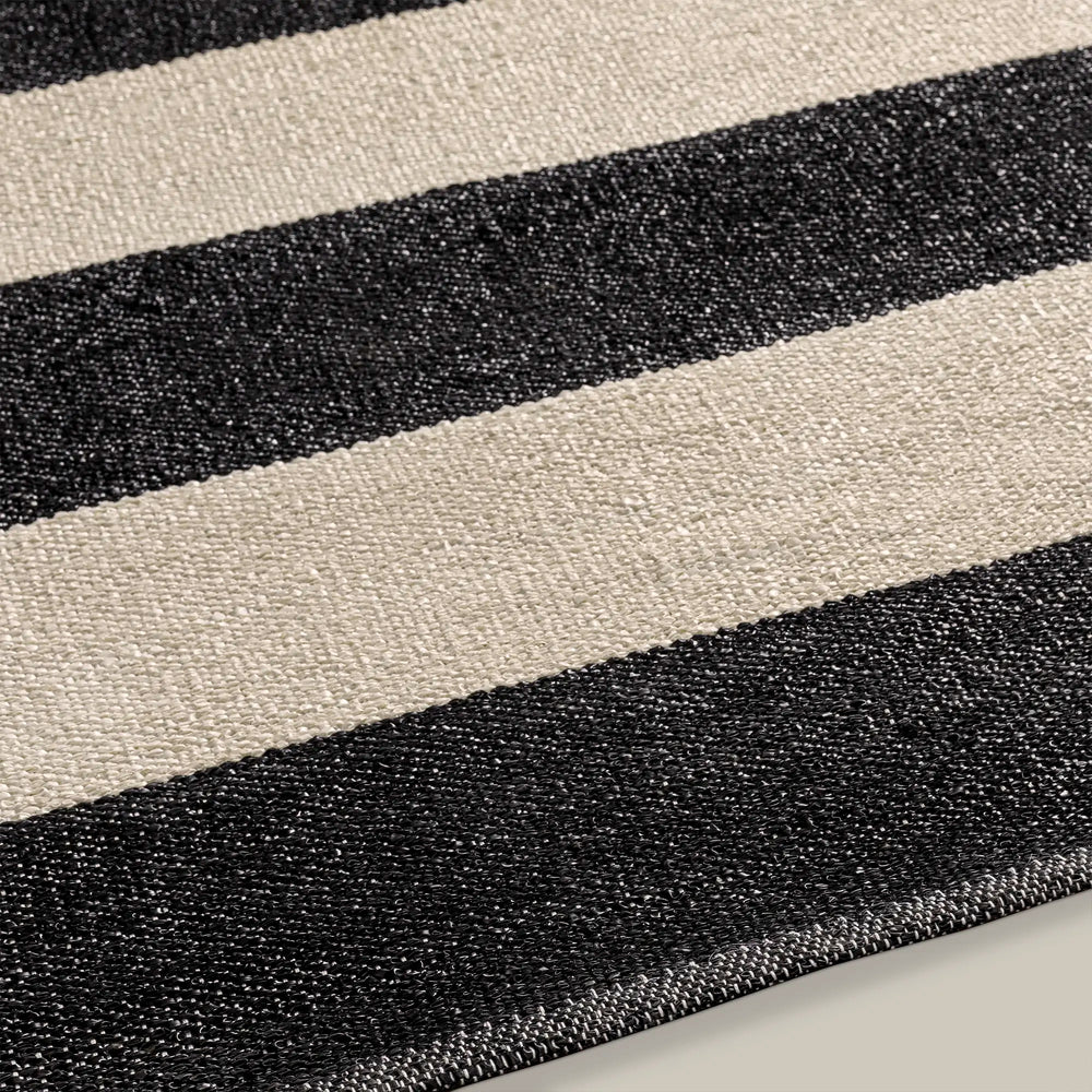 Lemieux et Cie Soraya Hand Woven Outdoor Rug in bold ivory and charcoal stripe pattern, close detail of woven texture and bound edge on neutral surface.