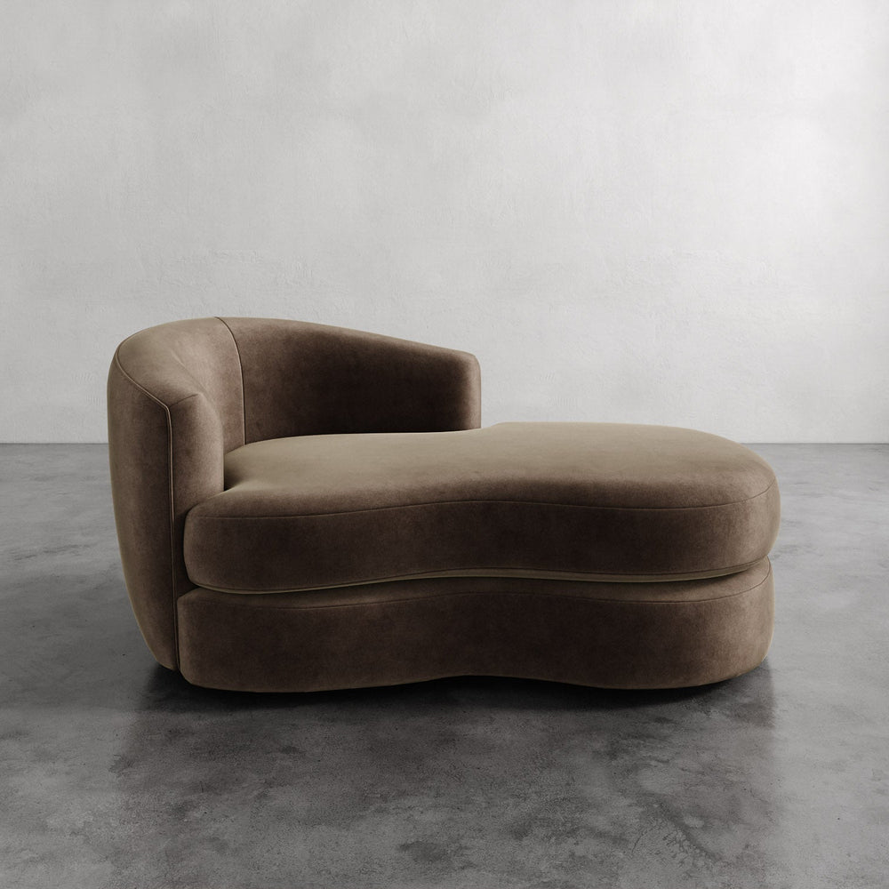 Lemieux et Cie Rulmann Left Arm Chaise in warm taupe, sculptural low-slung chaise with organic curved form, shown on concrete floor against neutral plaster walls.